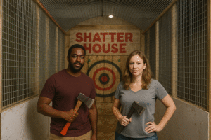 A man and woman standing in the Shatter House axe-throwing lane, each holding an axe in front of a wooden target.
